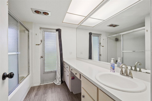 bathroom with a wealth of natural light, vanity, enclosed tub / shower combo, and hardwood / wood-style flooring