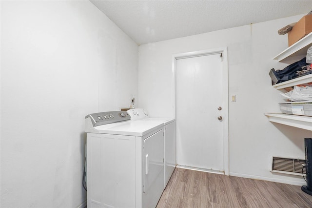 clothes washing area featuring light wood-type flooring, a textured ceiling, and washer and clothes dryer