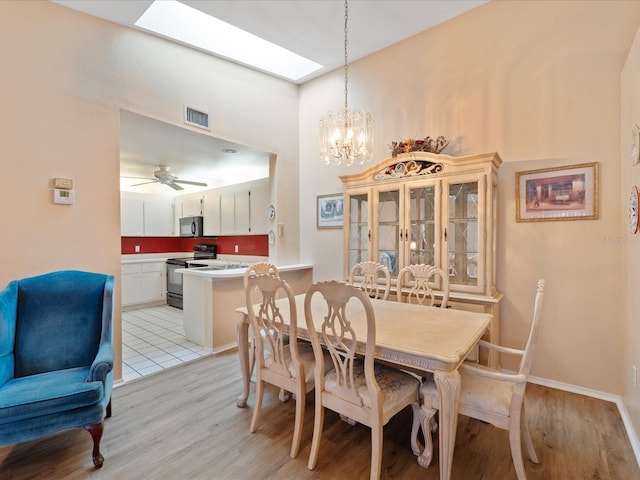 tiled dining area with ceiling fan with notable chandelier and a skylight