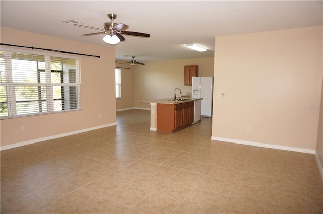 interior space with light tile patterned floors, sink, white refrigerator with ice dispenser, an island with sink, and ceiling fan