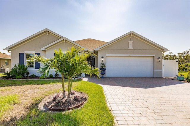 single story home with an attached garage, a front yard, decorative driveway, and stucco siding