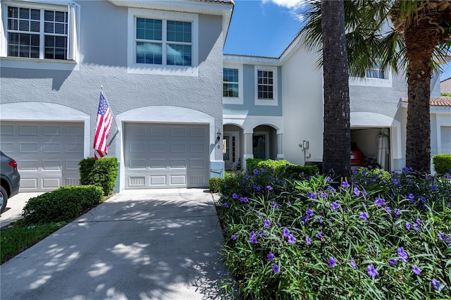 view of front of home with stucco siding, driveway, a tile roof, and a garage