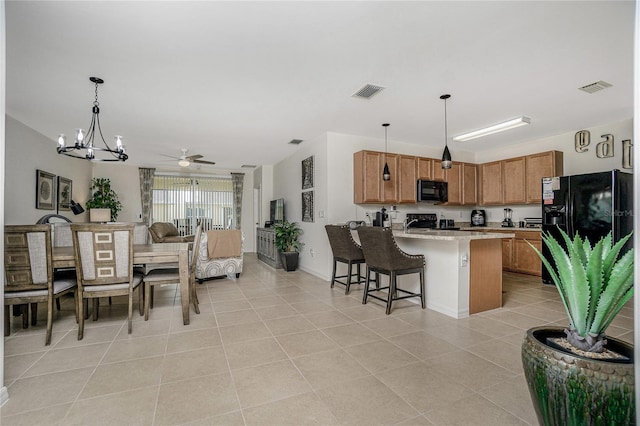 kitchen with a kitchen bar, ceiling fan with notable chandelier, light tile patterned floors, hanging light fixtures, and black appliances