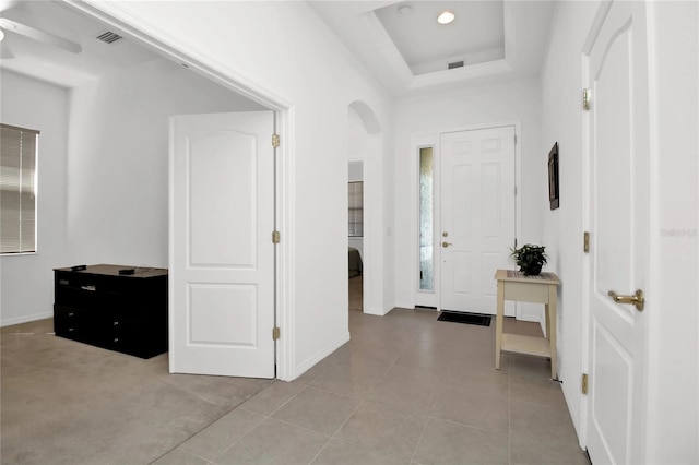 entryway with light tile patterned floors, a raised ceiling, and ceiling fan