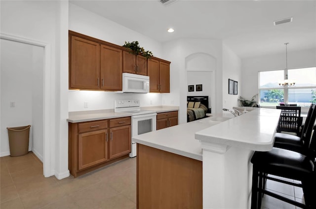 kitchen featuring sink, decorative light fixtures, white appliances, light tile patterned floors, and a breakfast bar area