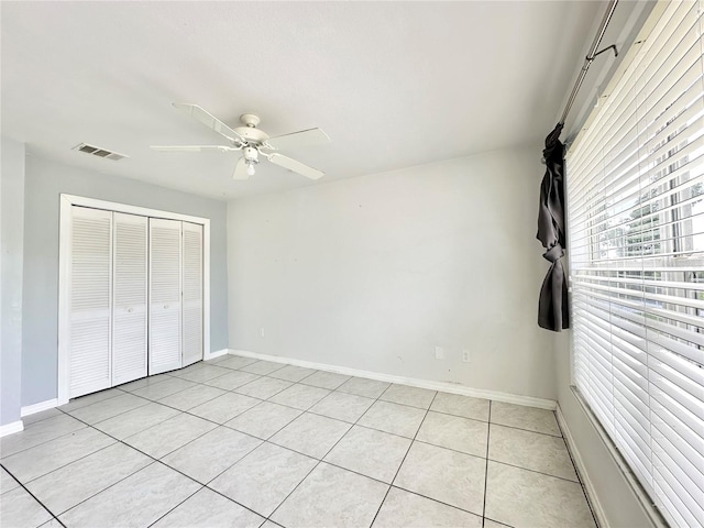 unfurnished bedroom with ceiling fan, a closet, multiple windows, and light tile patterned floors