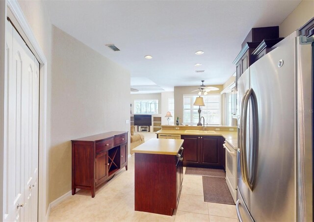 kitchen featuring sink, light tile patterned floors, white appliances, a kitchen island, and ceiling fan