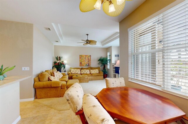 living room with ceiling fan, a tray ceiling, and light tile patterned floors