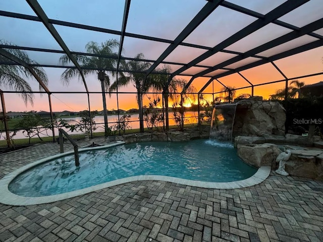 pool at dusk with a water view, a lanai, pool water feature, and a patio