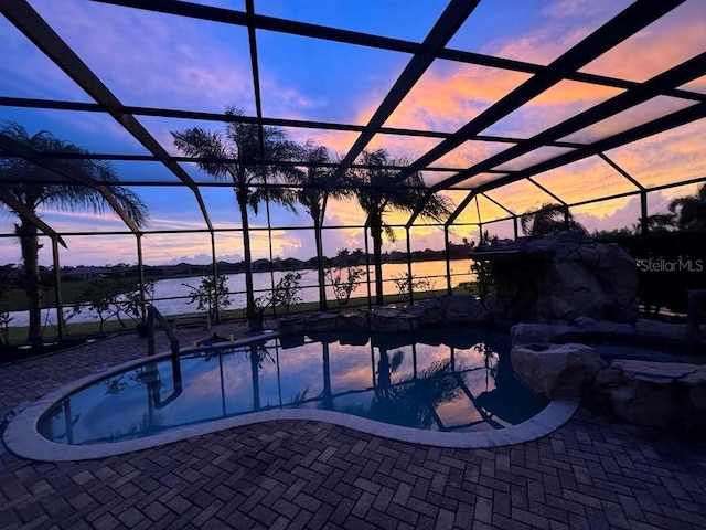 pool at dusk with a patio area, a lanai, and a water view