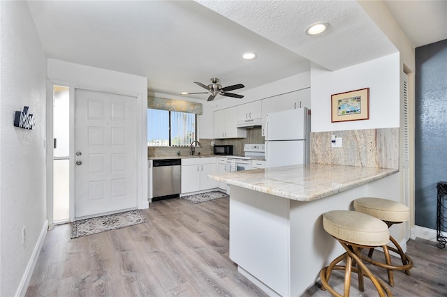 kitchen featuring kitchen peninsula, light wood-type flooring, a breakfast bar, white appliances, and white cabinets