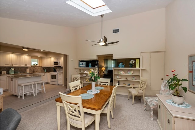 dining room with high vaulted ceiling, a skylight, visible vents, and ceiling fan