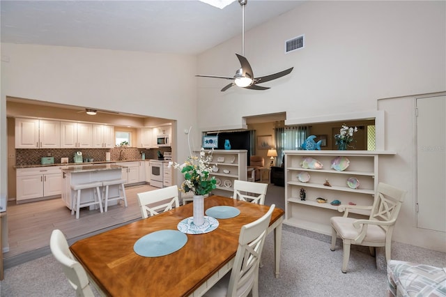 dining room with a ceiling fan, light wood-type flooring, visible vents, and high vaulted ceiling