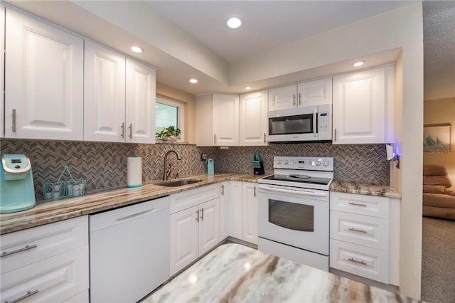 kitchen featuring white appliances, light stone counters, white cabinets, and a sink