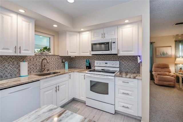 kitchen featuring light stone counters, visible vents, white cabinets, a sink, and white appliances