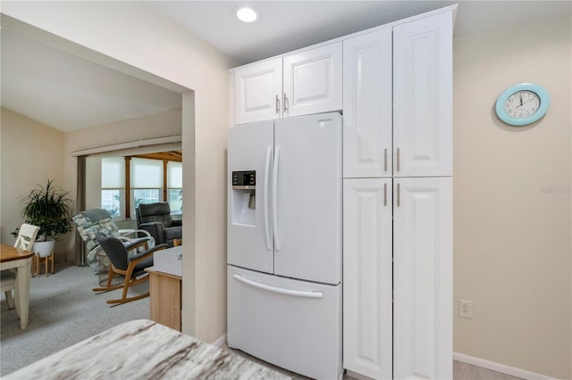 kitchen with light carpet, baseboards, white cabinets, light countertops, and white fridge with ice dispenser