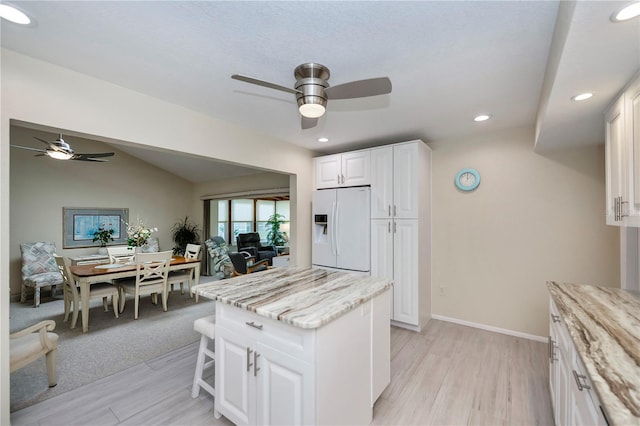 kitchen featuring light stone counters, open floor plan, white cabinets, vaulted ceiling, and white fridge with ice dispenser