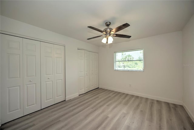 unfurnished bedroom featuring ceiling fan, light wood-type flooring, and multiple closets