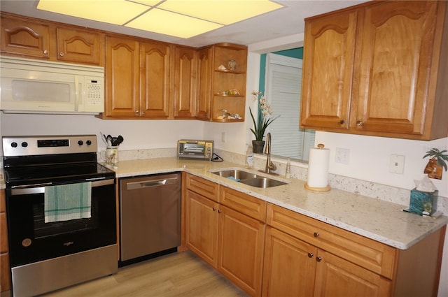 kitchen with light hardwood / wood-style floors, appliances with stainless steel finishes, sink, and light stone counters