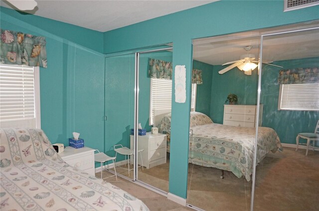 carpeted bedroom featuring ceiling fan, multiple windows, and multiple closets