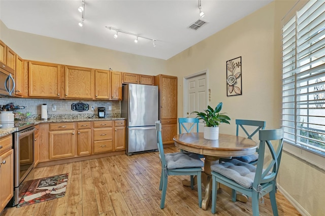 kitchen with tasteful backsplash, appliances with stainless steel finishes, light stone countertops, light hardwood / wood-style floors, and rail lighting