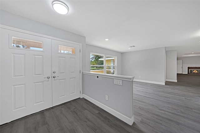 foyer entrance featuring dark wood-type flooring, visible vents, a lit fireplace, and baseboards