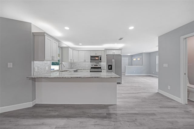 kitchen with light stone counters, backsplash, appliances with stainless steel finishes, a sink, and a peninsula