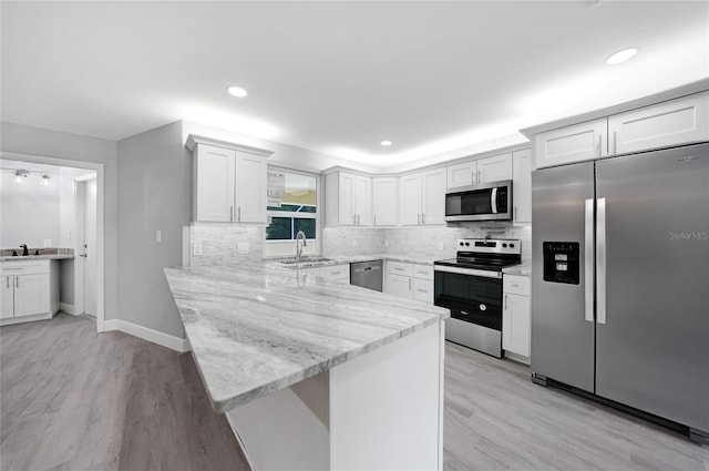 kitchen with stainless steel appliances, white cabinets, a peninsula, and light stone countertops