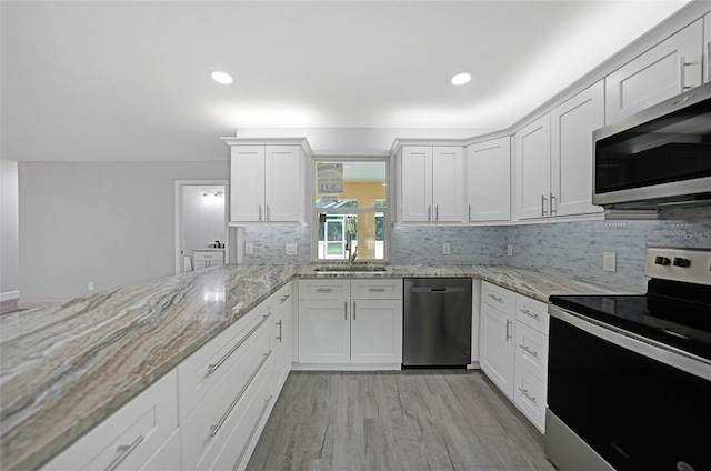 kitchen with light stone counters, a sink, white cabinets, appliances with stainless steel finishes, and light wood-type flooring