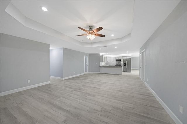 unfurnished living room featuring recessed lighting, a raised ceiling, light wood-style flooring, a ceiling fan, and baseboards