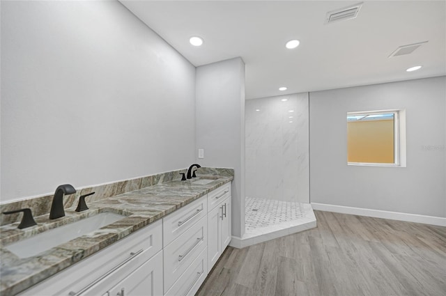 full bathroom with double vanity, a marble finish shower, a sink, and wood finished floors