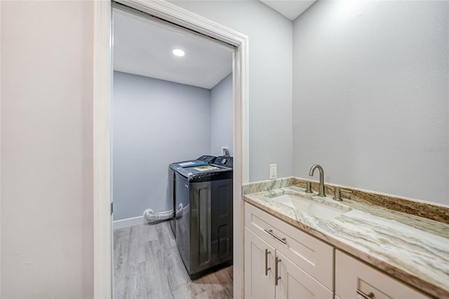 washroom with light wood finished floors, cabinet space, baseboards, washer and dryer, and a sink