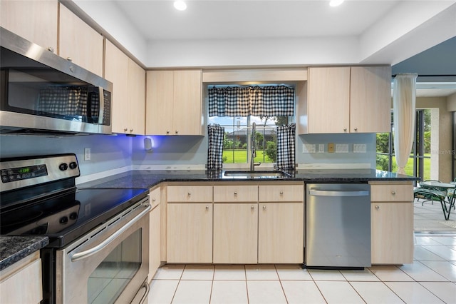 kitchen featuring appliances with stainless steel finishes, light tile patterned floors, dark stone countertops, and sink