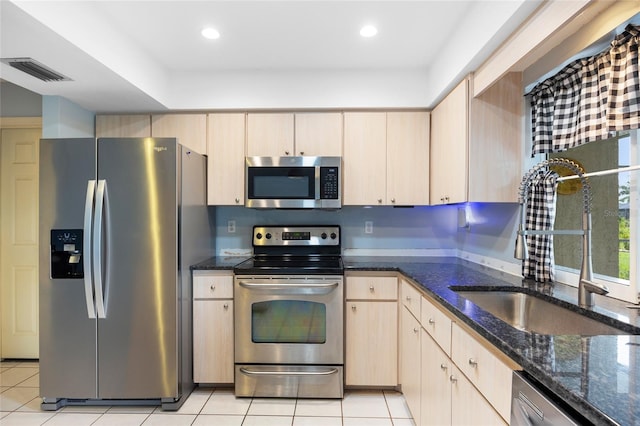 kitchen featuring stainless steel appliances, dark stone countertops, light tile patterned floors, and light brown cabinetry