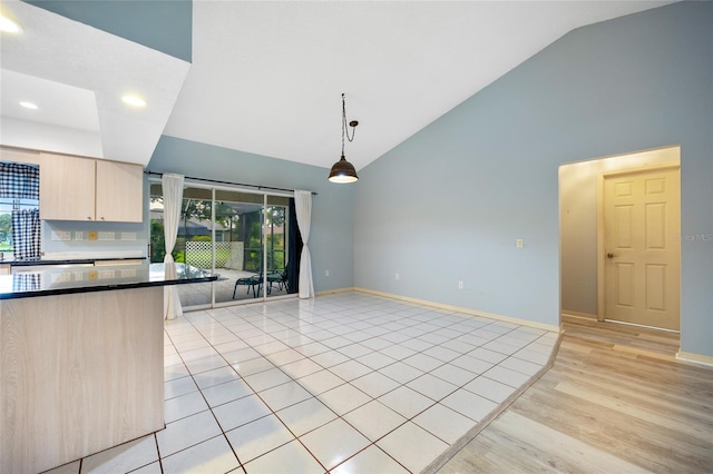 kitchen with light brown cabinetry, backsplash, light hardwood / wood-style floors, lofted ceiling, and pendant lighting