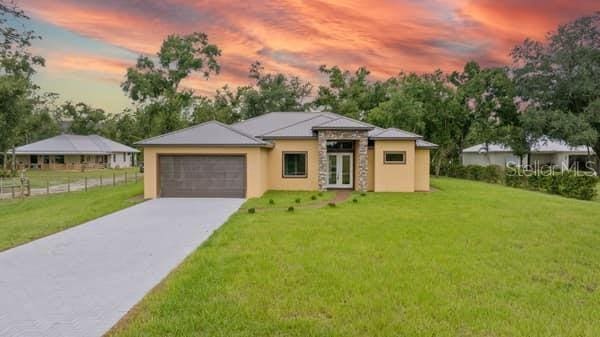 prairie-style house featuring stucco siding, a front lawn, french doors, concrete driveway, and an attached garage