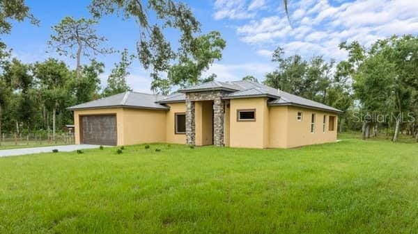 back of property with a yard, driveway, an attached garage, and stucco siding