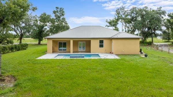rear view of house featuring a patio, a yard, a fenced in pool, and stucco siding