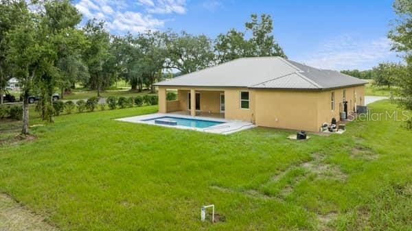 back of house featuring a patio, a yard, an outdoor pool, and stucco siding