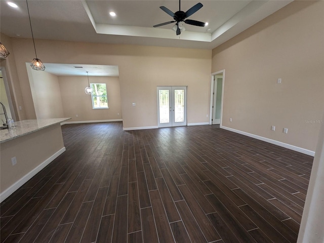 unfurnished living room featuring a towering ceiling, dark hardwood / wood-style flooring, a tray ceiling, ceiling fan, and sink