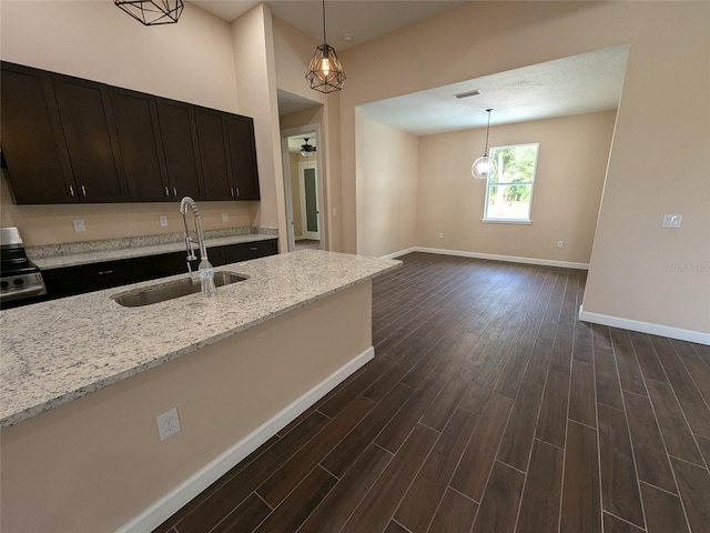 kitchen featuring light stone counters, sink, decorative light fixtures, dark wood-type flooring, and stainless steel range