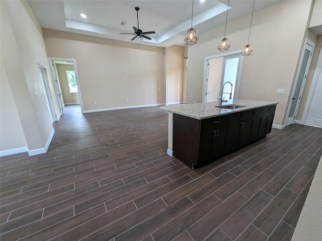 kitchen with dark wood-type flooring, light stone counters, a tray ceiling, ceiling fan, and sink