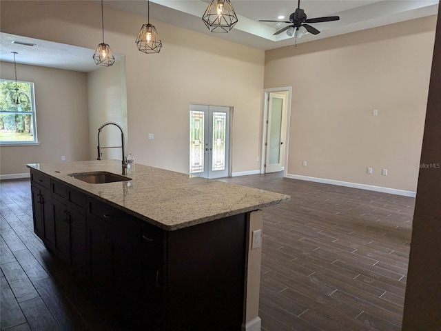 kitchen featuring light stone counters, an island with sink, dark hardwood / wood-style floors, and sink