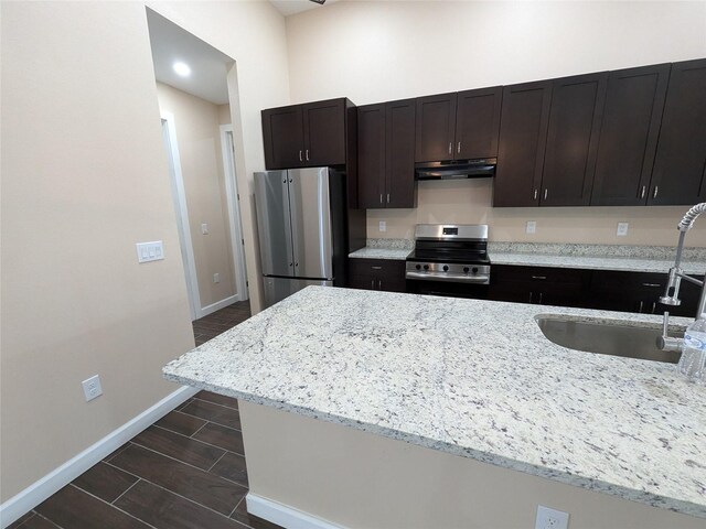 kitchen with light stone countertops, baseboards, a sink, under cabinet range hood, and appliances with stainless steel finishes