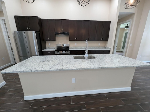 kitchen with ceiling fan, light stone counters, sink, a kitchen island with sink, and stainless steel appliances