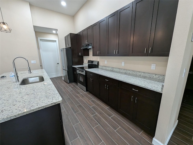kitchen with light stone countertops, wood finish floors, a sink, appliances with stainless steel finishes, and decorative light fixtures