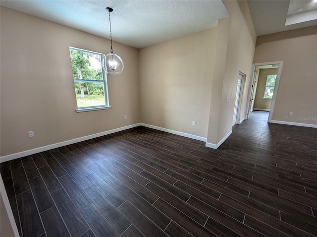 spare room with an inviting chandelier, dark wood-style floors, and baseboards