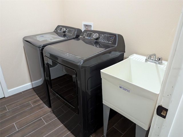 washroom with baseboards, wood finish floors, laundry area, a sink, and washer and clothes dryer