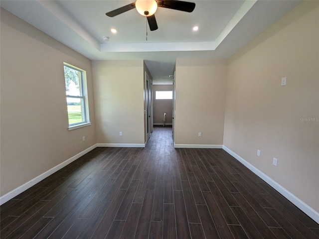 unfurnished room with ceiling fan, a tray ceiling, and dark wood-type flooring