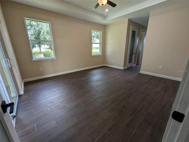 empty room featuring baseboards, a tray ceiling, ceiling fan, and dark wood-style flooring